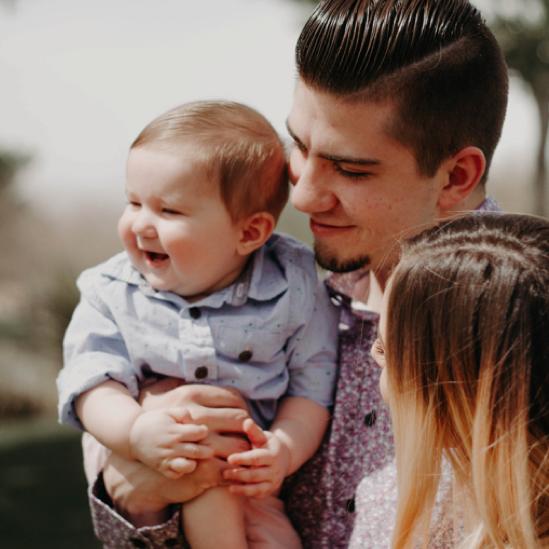 Two young parents holding their smiling baby in a blue button up shirt